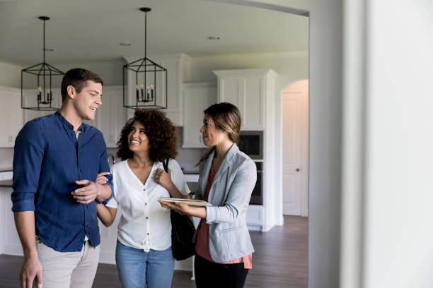 Young couple smile as they talk with a female real estate agent. The real estate agent is showing them a new home.